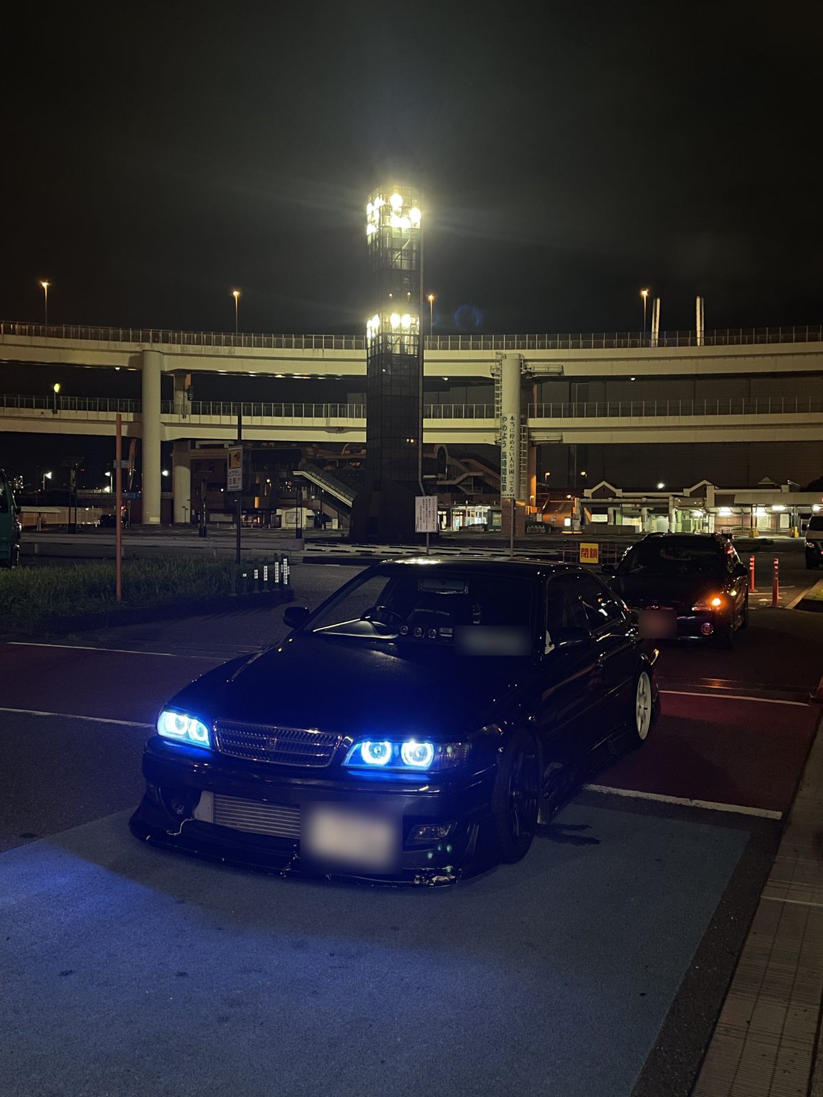 A dark blue Toyota Chaser JZX100 parked at Daikoku PA at night, with a red closed sign behind it