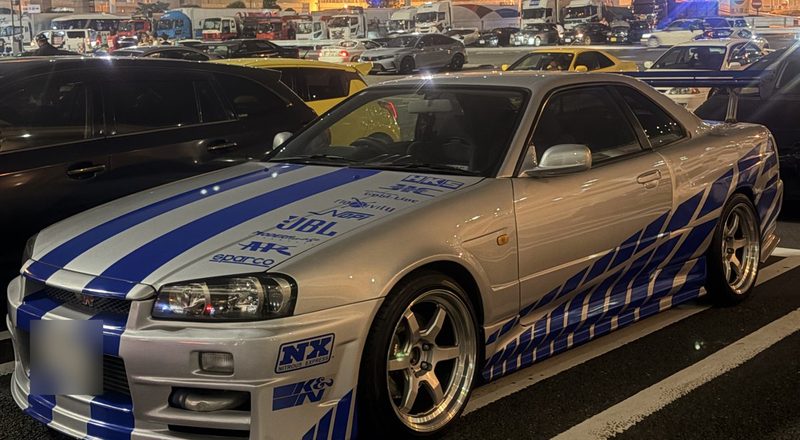 A blue Nissan Skyline R34 in Fast and Furious style livery parked at Daikoku PA at night